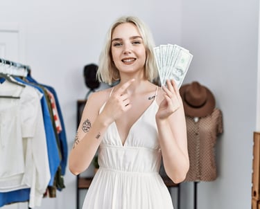 Mujer sonriente sosteniendo dinero en efectivo y señalando billetes de dólar en una tienda de ropa.