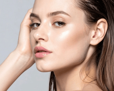 A close-up of a young woman showing off her glowing skin and natural makeup look.