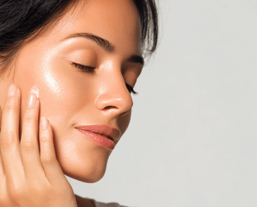 A woman applying moisturizing face cream to her glowing, hydrated skin for a skincare routine.