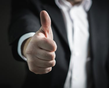Professional businessman in a dark suit giving a thumbs up gesture for success and approval.