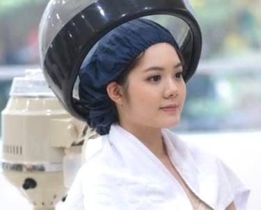 A young woman with a hair bonnet sitting under a professional salon hooded hair dryer for a treatment.