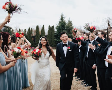 Smiling bride and groom walk through a cheering wedding party holding vibrant floral bouquets.