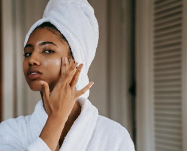 A woman is rubbing moisturizer into her cheek.