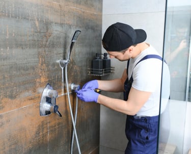 Technician wearing cap and gloves adjusting shower valve on brown tiled wall