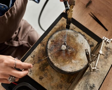Un joyero usa un soplete para soldar un anillo de plata sobre una mesa de trabajo