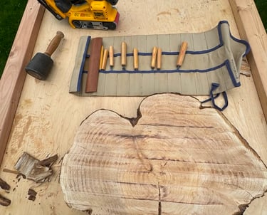 Large table with belt sander, wood knives, and live edge piece of wood