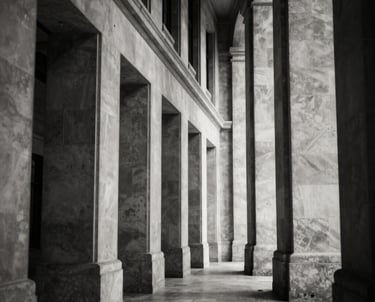 A black and white architectural shot of a corridor in a high court building, showing strong repetitive lines and a sense of order. High contrast with deep navy-like blacks and warm off-white highlights.