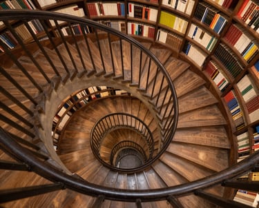 A wooden spiral staircase winds down through a library with circular built-in bookshelves.