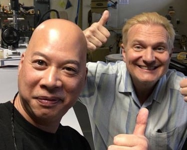Ray and Jeff Hobson giving thumbs up in a woodworking workshop with power tools in the background.
