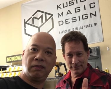 Ray and Mark Kalin standing in front of a Kustom Magic Design banner in a Las Vegas workshop.