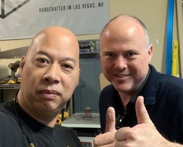 Ray and Chris giving a thumbs up in a Las Vegas woodworking shop with tools and equipment.