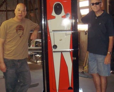 Two men standing next to a vintage Zig Zag Girl magic illusion cabinet in a workshop.