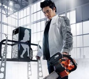 Professional magician holding an orange chainsaw next to a modern stage illusion prop in a bright studio.