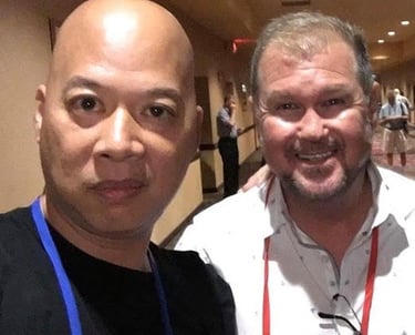 Ray Lum and Daniel Summer taking a selfie together at a conference event in a hotel hallway.