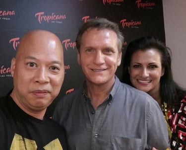 Three people smiling at a Tropicana Las Vegas event with a branded logo backdrop.
