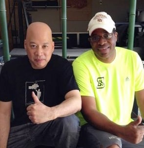 Two men posing for a photo at the gym, giving a thumbs up while wearing athletic gear.