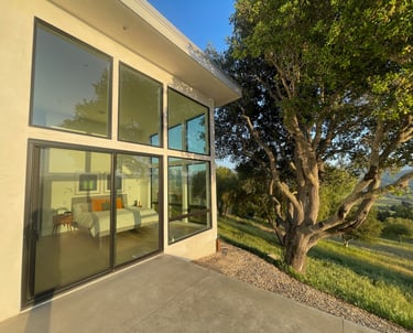 Modern luxury bedroom with floor-to-ceiling glass windows and sliding doors overlooking a lush hillside.
