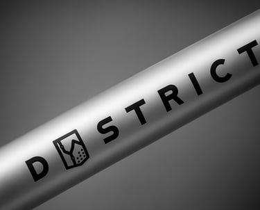 A close-up of a silver aluminum bike frame tube featuring the District brand logo in black text.