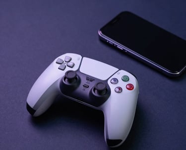 A clean, minimalist studio shot of a white gaming console controller and a mobile phone on a deep navy surface. Elegant composition with soft purple shadows.