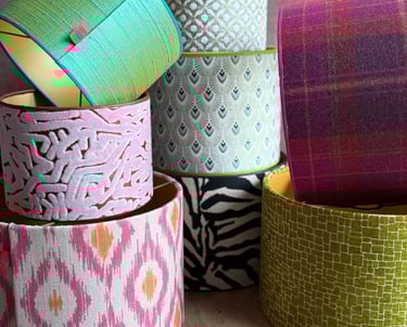 A colorful stack of decorative drum lampshades featuring ikat, plaid, and animal print fabrics.