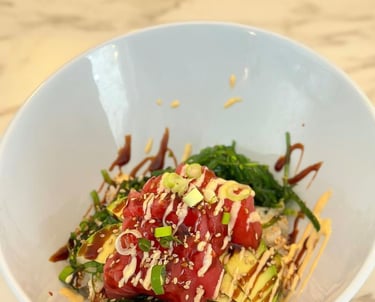 Fresh tuna poke bowl with avocado, seaweed salad, spicy mayo, and sesame seeds in a white bowl.