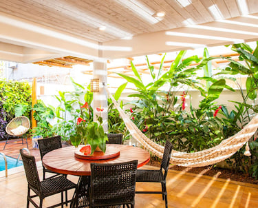 table and chairs in bright room with tropical plants, a hammock, and a pool