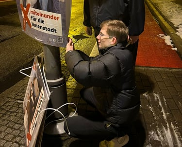Junger Mann befestigt Wahlplakat an Laternenmast bei Nacht – politisches Engagement
