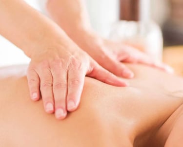 Massage therapist applying pressure to patient's upper back during therapeutic massage. 
