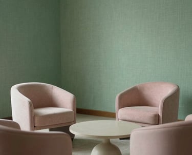 A serene pedagogical consulting room with elegant minimalist furniture, soft green linen textures, and soft pink accents, Southern European / Italian aesthetic.
