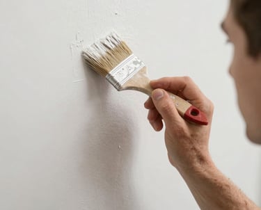 A smiling painter carefully applying a vibrant blue coat to a modern home's exterior wall on a sunny day.