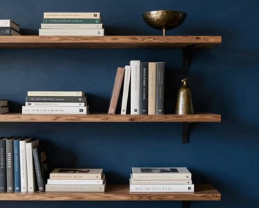 Minimalist bookshelf with design books and a small bronze sculpture. Soft shadows, deep blue wall, Latin American / Hispanic sophisticated interior.