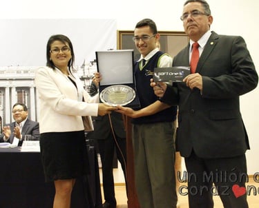 A smiling student receives an academic award and a SoftOne gift from officials at a formal ceremony.