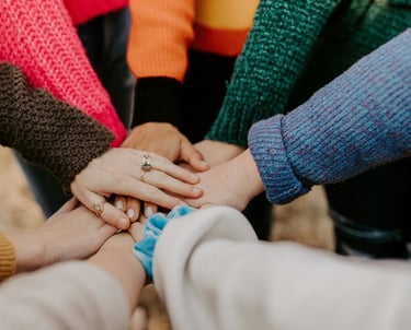 Diverse group of woman in colorful sweaters joining hands in a huddle for community support.