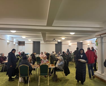 Diverse group of people enjoying a community meal and social gathering in a large hall.