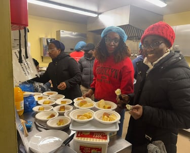 Smiling volunteers serving portions of cake and ice cream at a community soup kitchen event.