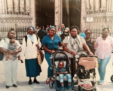 A group of African women and children posing in front of the ornate stone entrance of Notre-Dame de Paris.