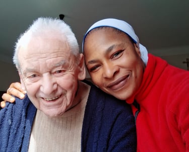 A smiling elderly man and a happy female caregiver in a red jacket posing for a close-up portrait.