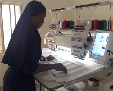 A nun uses a multi-head industrial embroidery machine to sew patterns on white fabric in a workshop.
