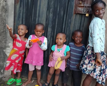 Five happy young African children posing together in front of a dark metal door outdoors.