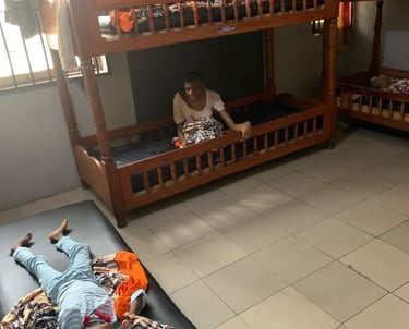 A shared bedroom with wooden bunk beds and a child lying on a floor mattress.