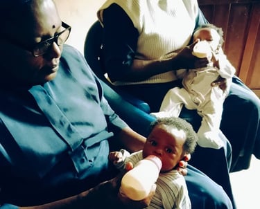 African Catholic nuns bottle-feeding two young infants at a childcare mission or orphanage center.