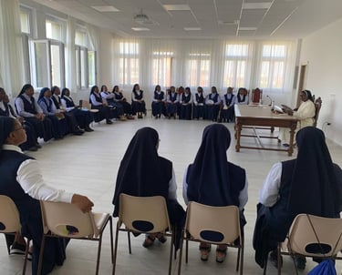 Catholic nuns in habits gather for a meeting in a bright seminar room with large windows.