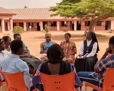 A group of diverse community members sitting in a circle for a meeting at an African school courtyard.