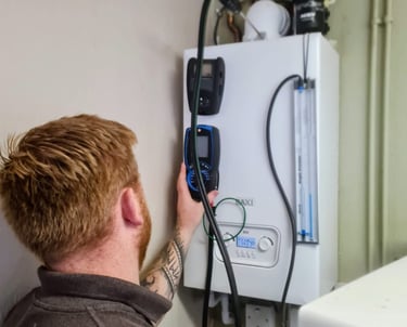 A heating engineer performs a gas boiler service and safety inspection using a digital flue gas analyzer.