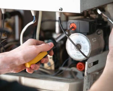 A technician using a screwdriver for professional boiler repair and heating system maintenance.