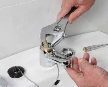 Plumber using an adjustable wrench to repair a leaking bathroom sink faucet.