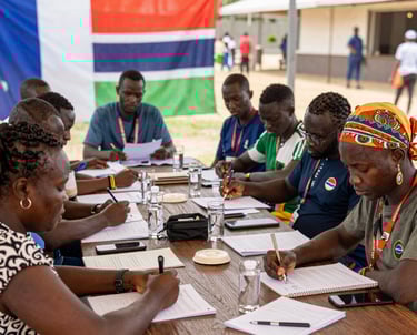 A group of Gambian and French professionals collaborating around a table with documents and laptops.