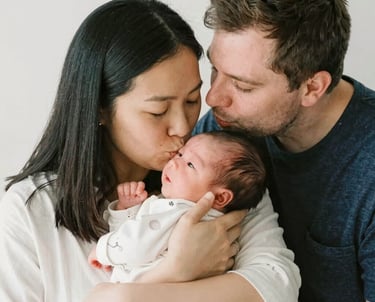 A gentle registered nurse warmly supporting a smiling mother and her newborn in a softly lit home setting.