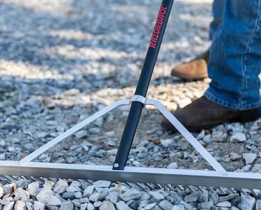 Close-up of a grading rake leveling a gravel base for a stable interlocking stone foundation.