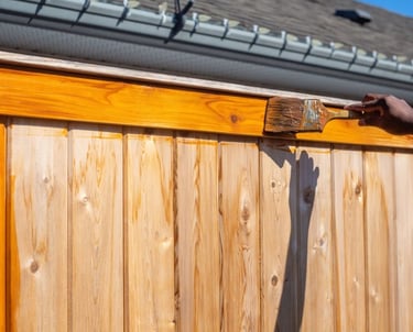 Professional application of golden oak wood stain on a horizontal privacy fence border.